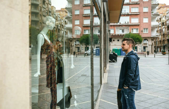 Young man with shopping bags looking at a shop window to buy a gift